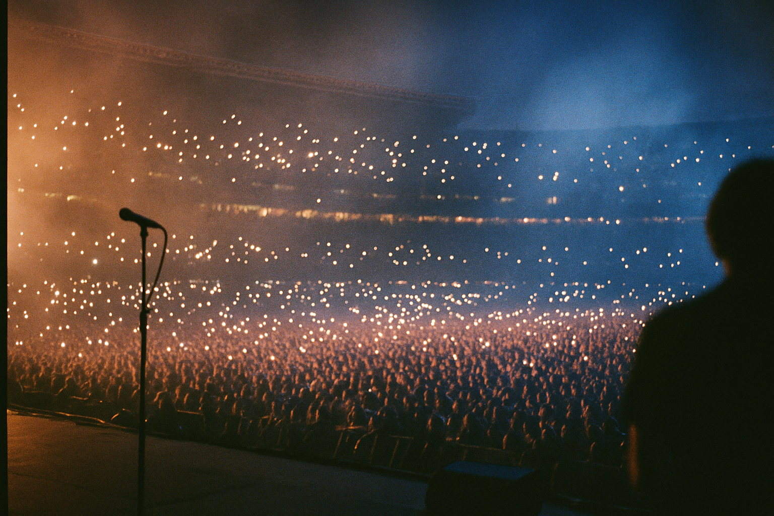 View from the stage over a stadium crowd lit by phone lights